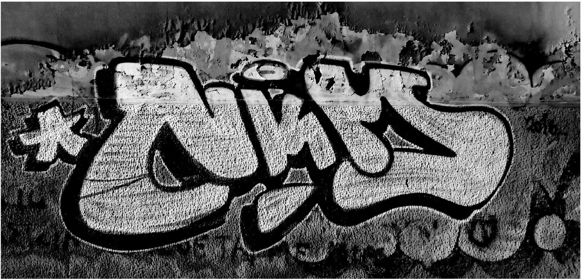 Black and white NKMS graffiti piece on a weathered wall, with a star on the left